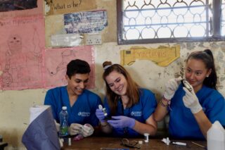 Group of medical interns in blue scrubs posing for a group photo outside Makande Girls' Secondary School during a global health outreach program.