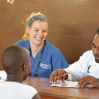 Group of medical interns in blue scrubs posing for a group photo outside Makande Girls' Secondary School during a global health outreach program.