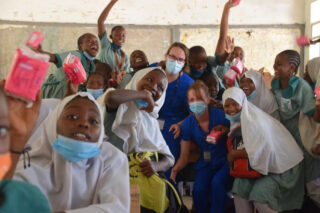 Group of medical interns in blue scrubs posing for a group photo outside Makande Girls' Secondary School during a global health outreach program.