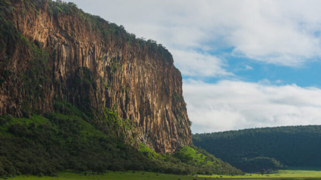 A dramatic cliff face with lush greenery, possibly in an East African landscape, ideal for east africa safari tours.