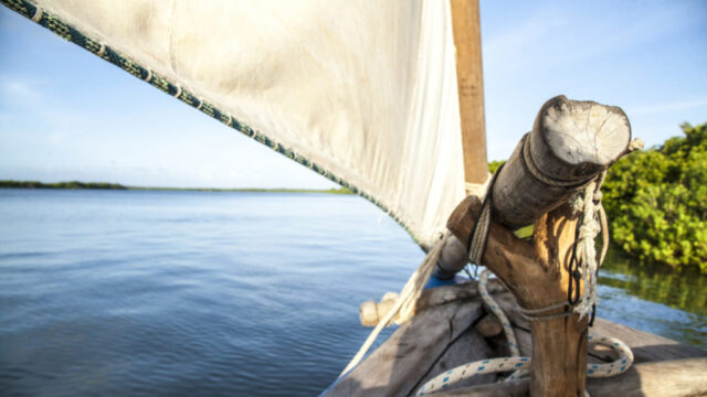 A traditional wooden sailboat on a calm body of water, suggesting serene travel or exploration.