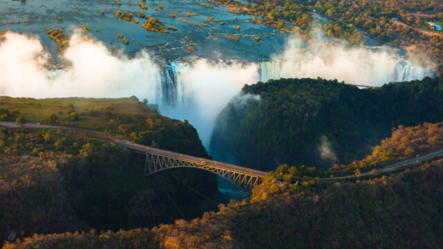 Aerial view of Victoria Falls with a bridge and mist rising from the cascading water.
