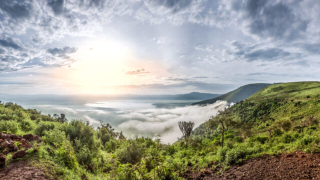 A breathtaking view of lush green hills, a vast valley, and a misty horizon at sunrise, ideal for east Africa safari tours.