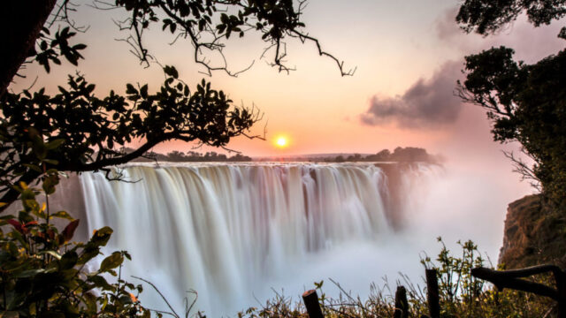 A stunning view of a large waterfall at sunset, surrounded by lush foliage.