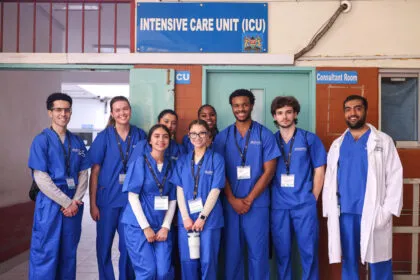 A group of people in blue scrubs posing in front of an intensive care unit sign