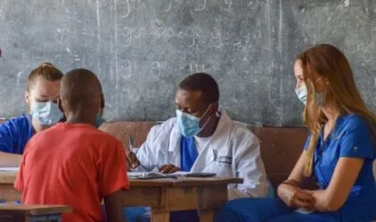 A group of medical professionals wearing masks is interacting with a child in a classroom setting.