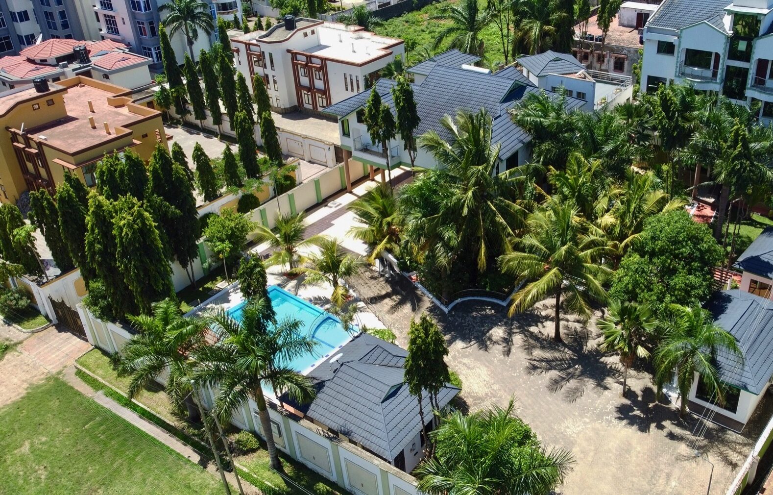 Aerial view of a residential area with a swimming pool, palm trees, and several houses.