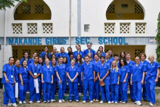 Group of medical interns in blue scrubs posing for a group photo outside Makande Girls' Secondary School during a global health outreach program.