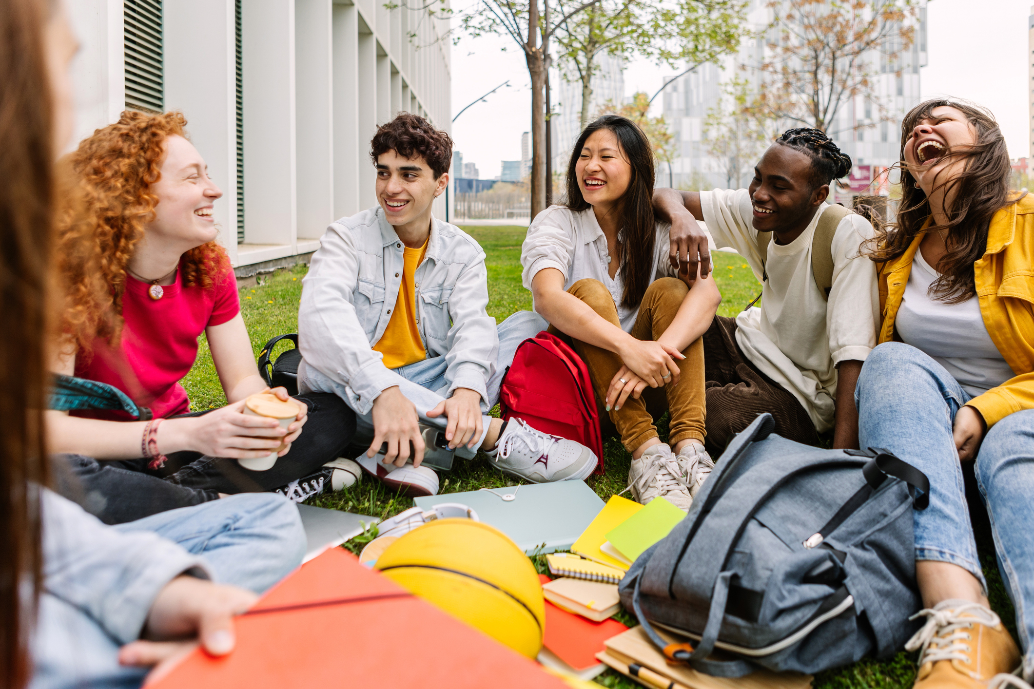 A group of young adults sitting on grass near a building, enjoying each other's company.