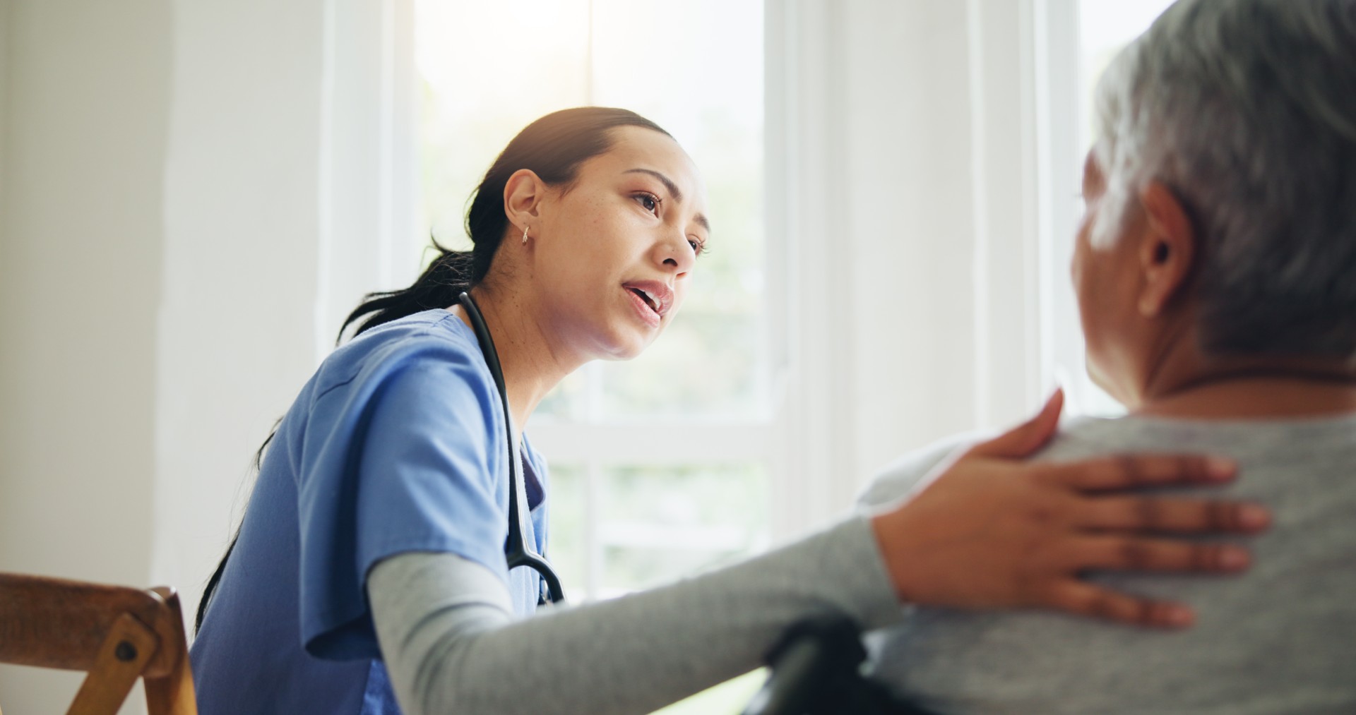 A healthcare professional is speaking compassionately with a patient, placing a hand on their shoulder.