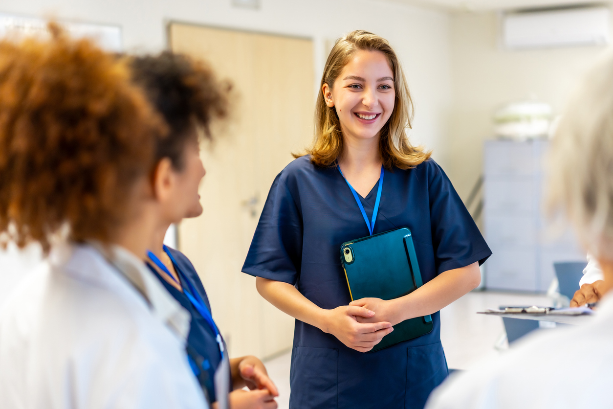 A group of people in medical attire are gathered, with one person smiling and holding a folder.