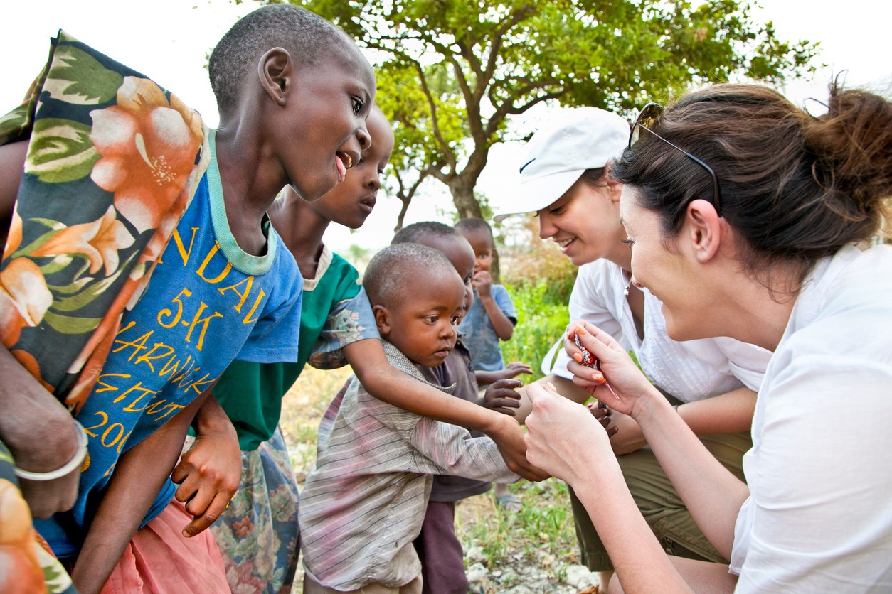 People interacting joyfully outdoors, with some laughing and others smiling, appearing to be in a rural setting.