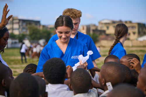 A group of people in blue uniforms are interacting with children outdoors.