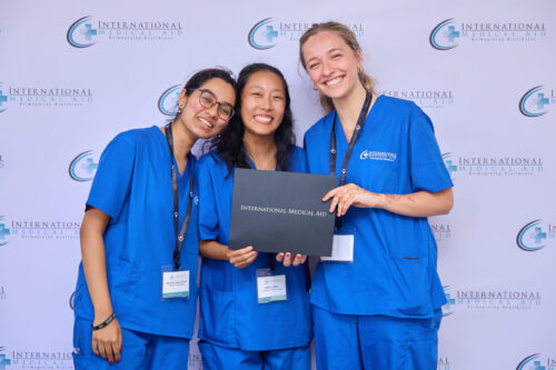 Three people in blue scrubs holding a certificate from International Medical Aid and smiling at the camera.