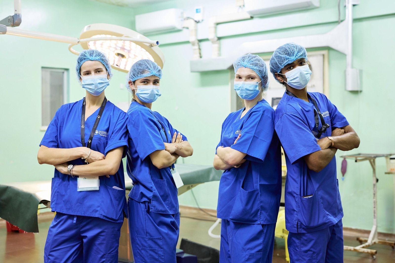 Four International Medical Aid interns in blue scrubs, caps and masks standing with arms crossed in a hospital operating room in Mombasa, Kenya