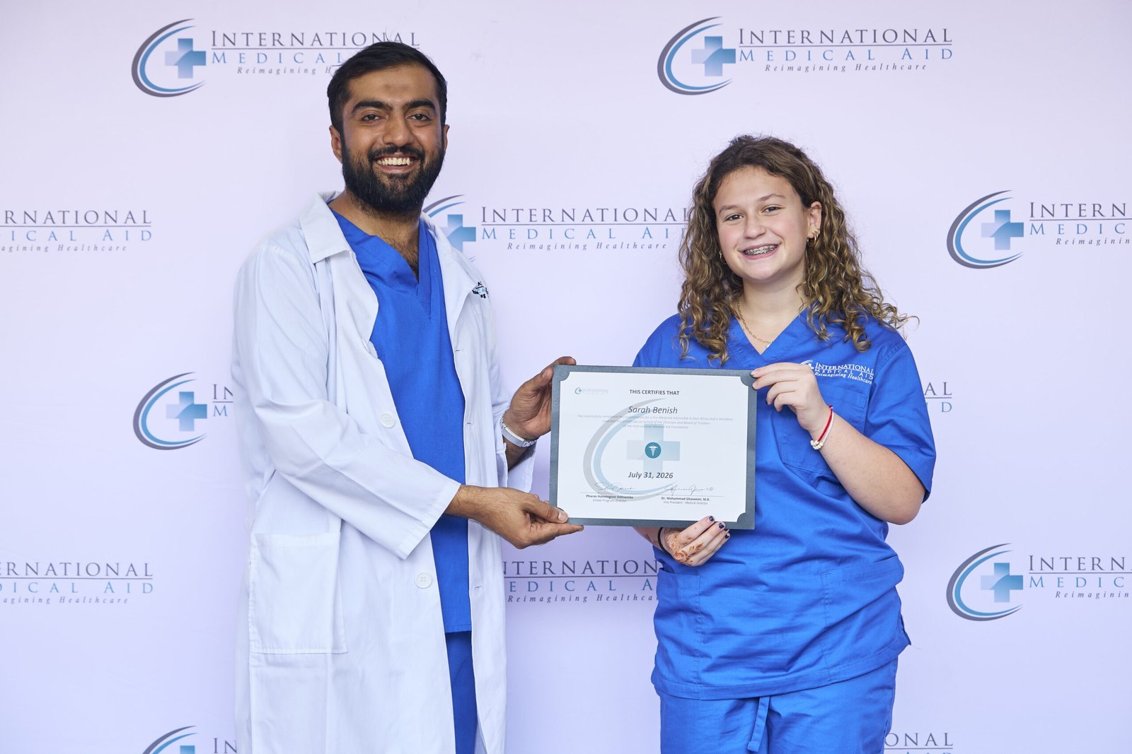 Sarah Benish in IMA scrubs holding her International Medical Aid internship certificate with Dr. Shazim Bagha