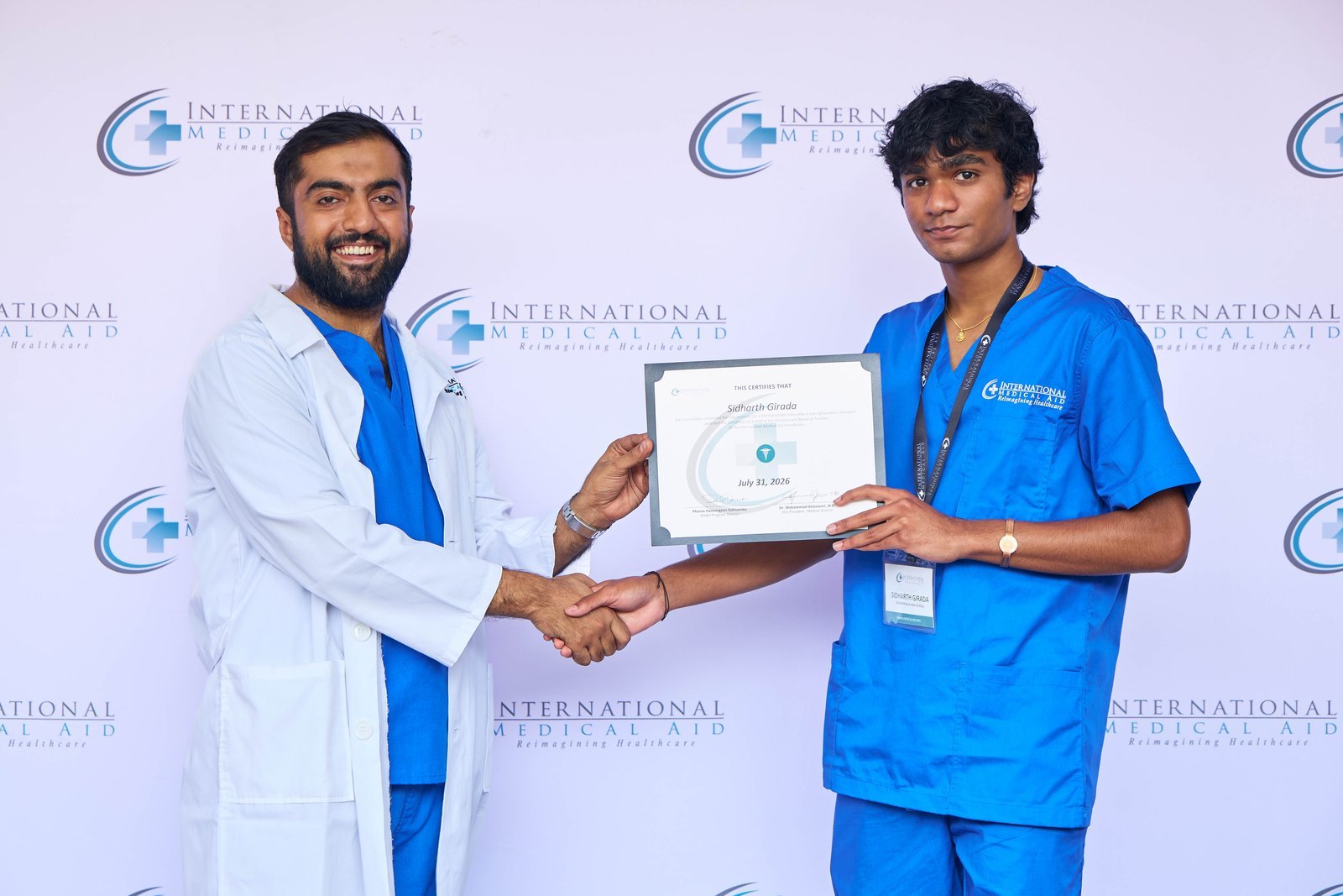 Sid Girada in IMA scrubs shaking hands with Dr. Shazim Bagha while receiving his International Medical Aid internship certificate