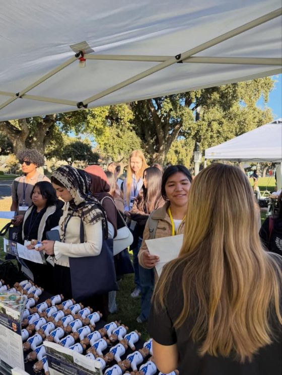An IMA representative talking with a line of students at the IMA booth under a white tent